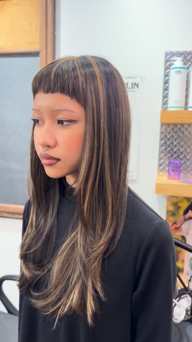 Woman with long black hair and light brown highlights sitting in a salon