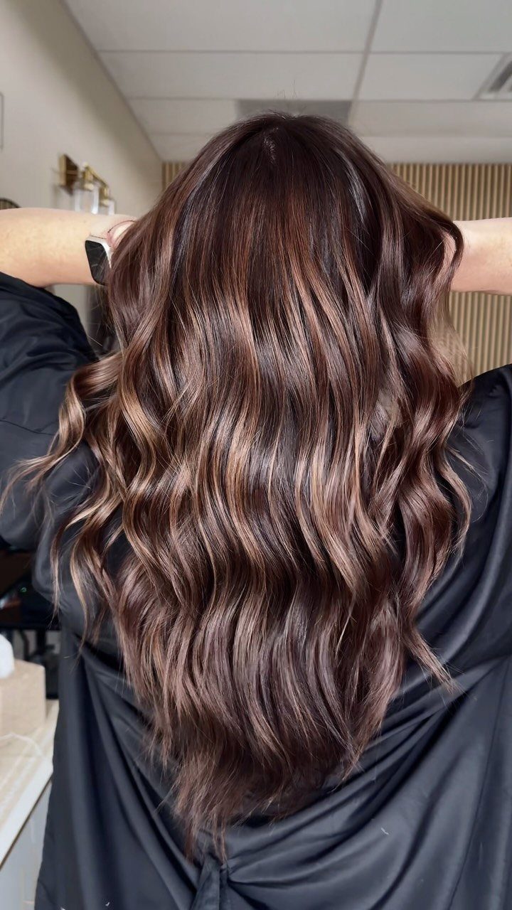 Long wavy dark brown hair shows subtle reddish mahogany highlights in a salon