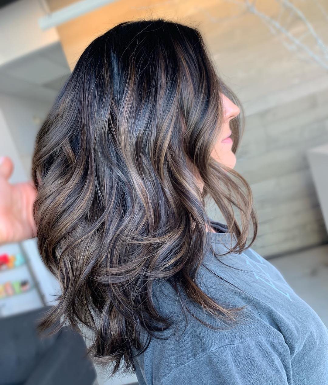 Wavy dark hair with cool mocha balayage highlights in a salon