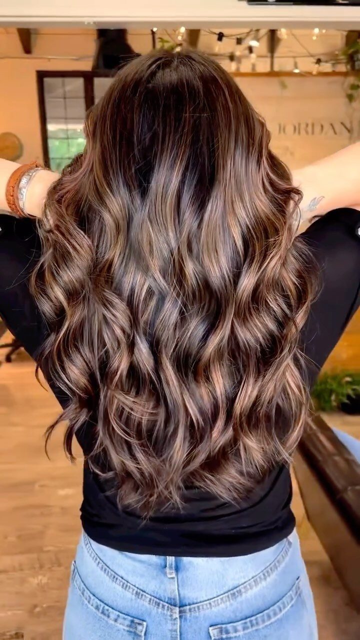 Long dark brown waves with soft, lighter brown highlights in a salon