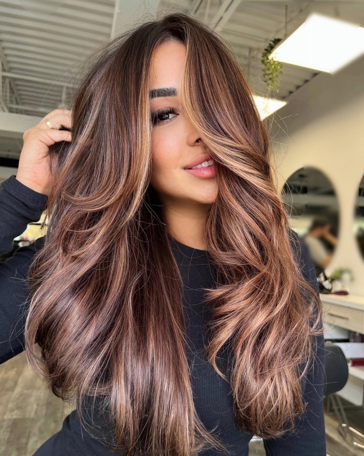 Woman displaying long dark hair with voluminous warm brown balayage highlights