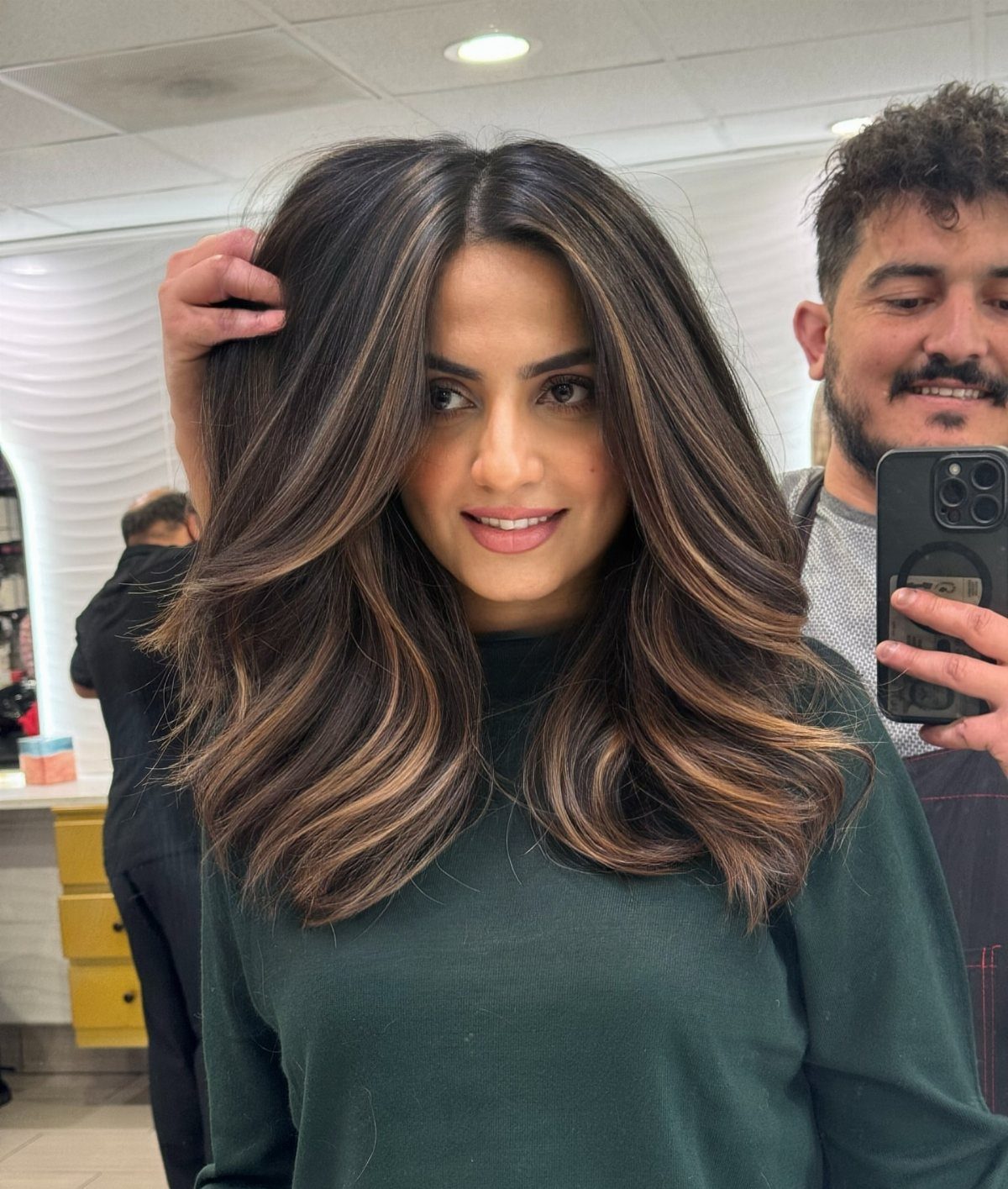 Woman showing long dark waves with warm golden-brown highlights in a salon