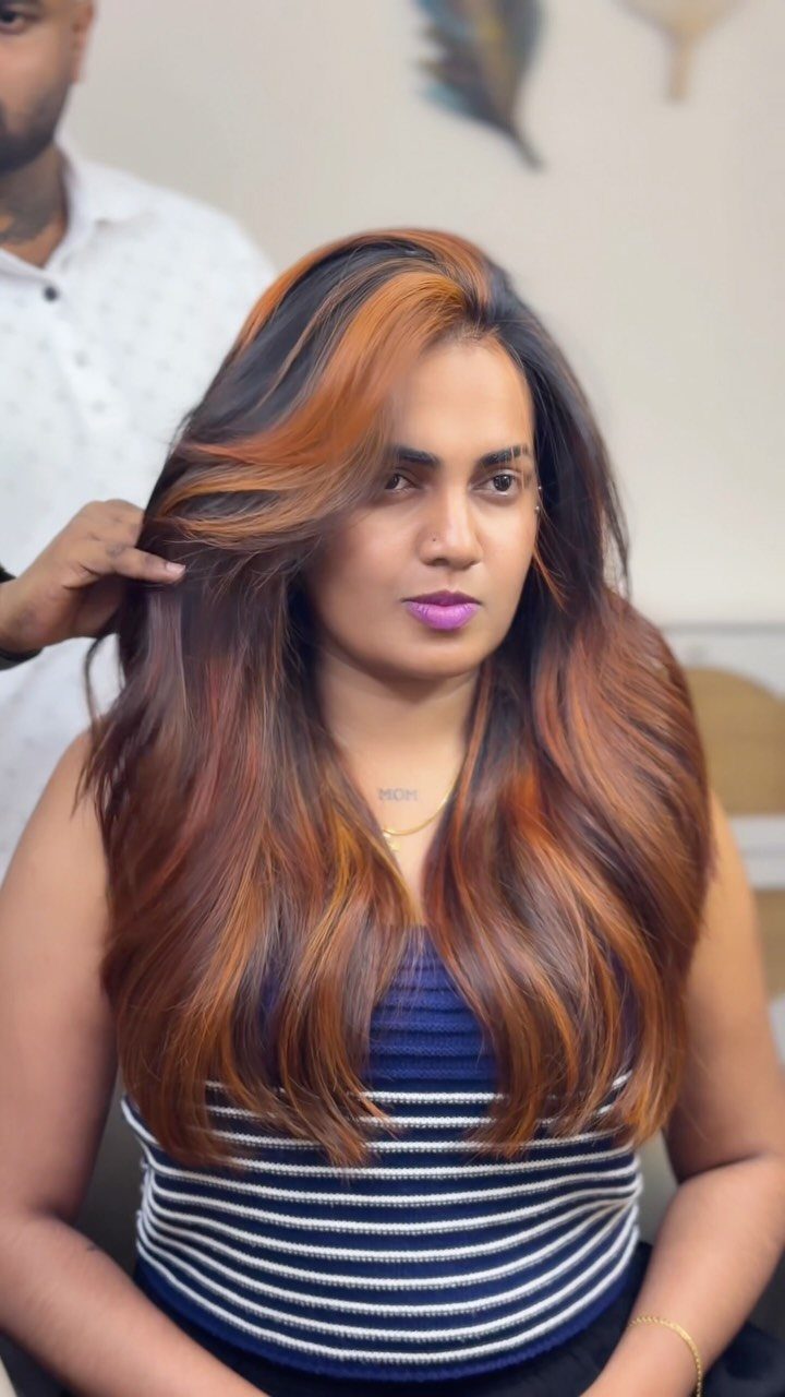 Long straight black hair with broad golden copper streaks framing a seated woman’s face