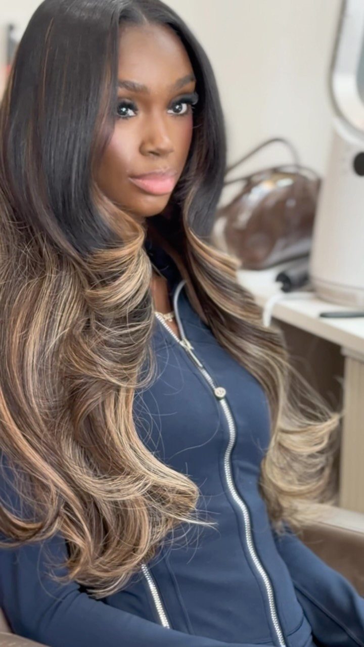 Woman with long glossy black waves and broad honey-blonde highlights