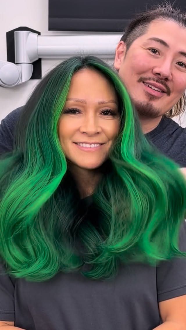 Long black waves with vivid neon-green face-framing highlights in a salon
