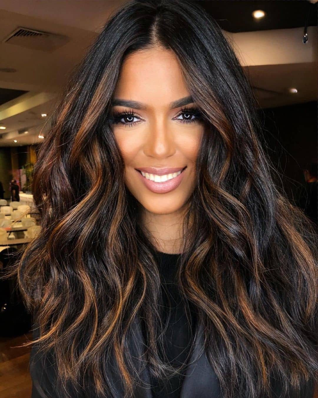 Woman smiling with long, wavy dark hair and warm brown highlights