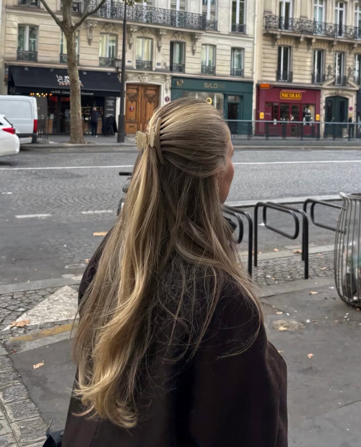 Long blonde waves gathered half-up with a cream claw clip on a city sidewalk