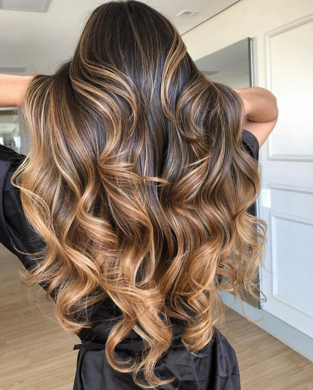 Long brunette curls display warm honey-caramel highlights throughout the hair