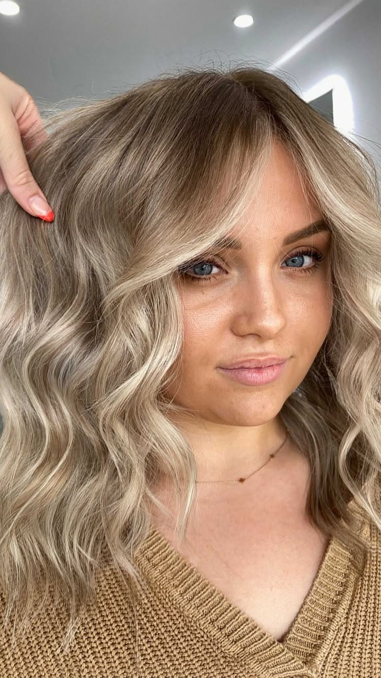 Woman showing long, wavy mushroom blonde hair with darker roots