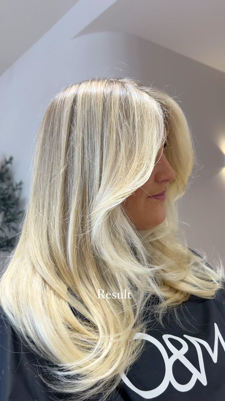 Long platinum blonde balayage hair with darker roots, layered waves, and a sweeping fringe