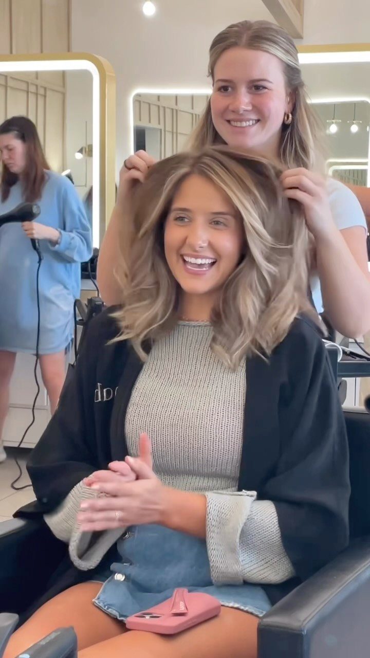 Woman with wavy beige-blonde hair and warm brunette roots in a salon chair
