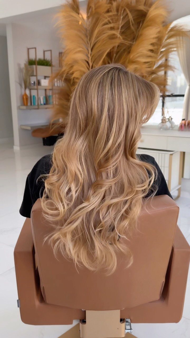 Long blonde waves with darker roots cascading over a brown chair in a salon