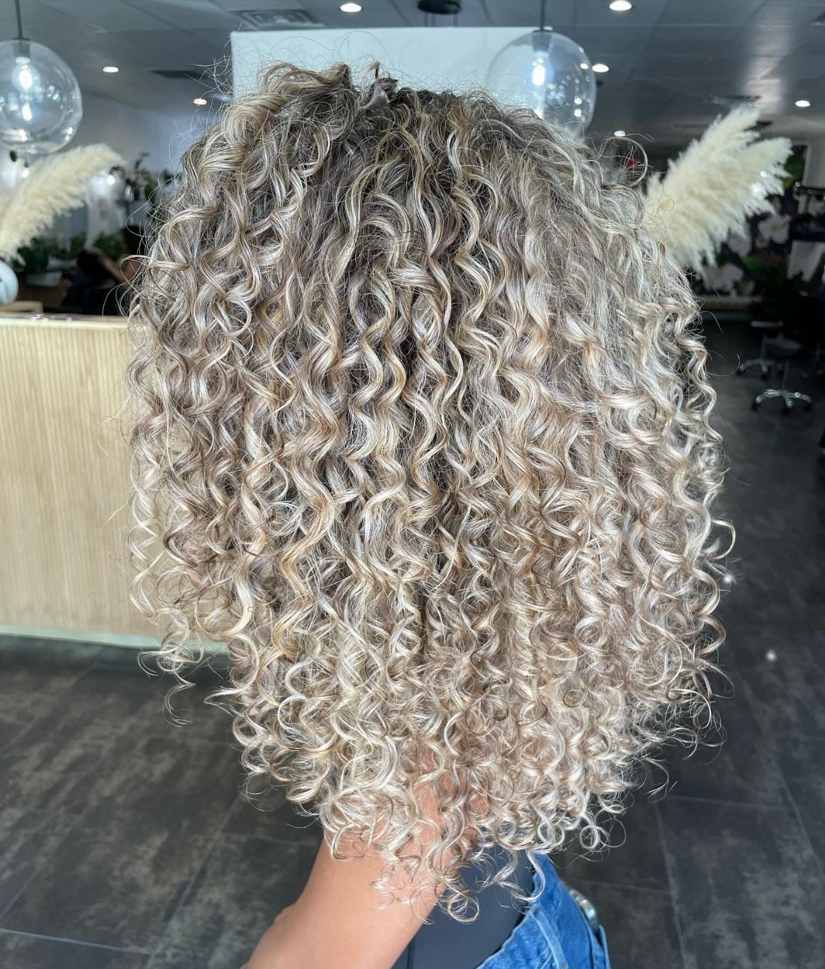 Short champagne-blonde curls with dark ash-brown roots in a salon
