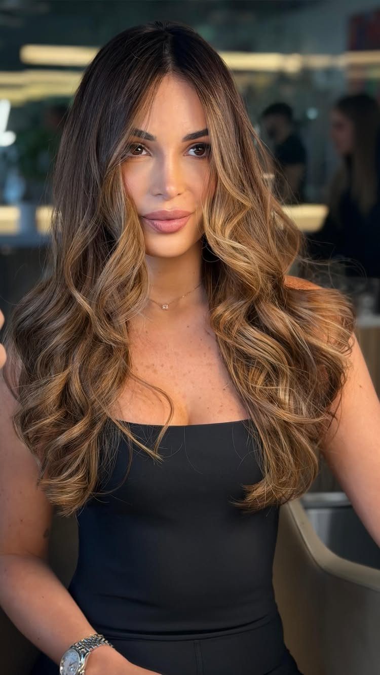 Woman with long dark curls and warm caramel honey highlights