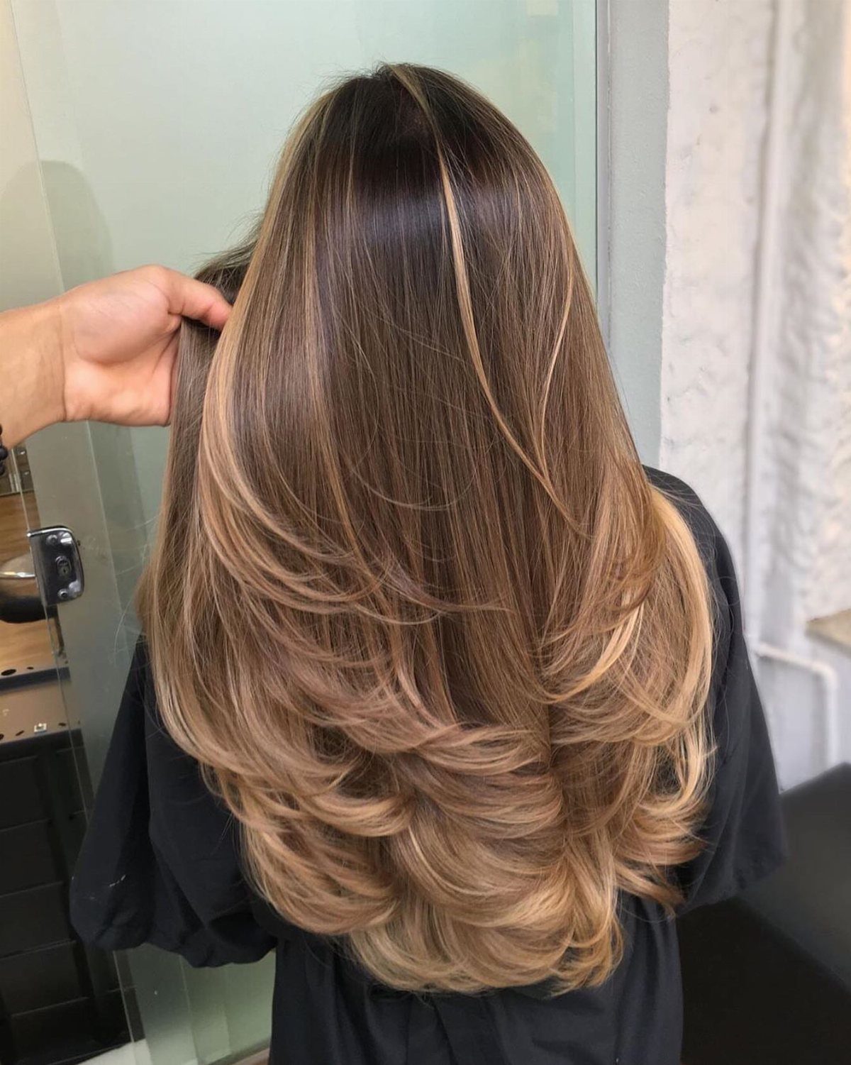 Long rooted brown hair blends into warm caramel honey highlights and curled ends.