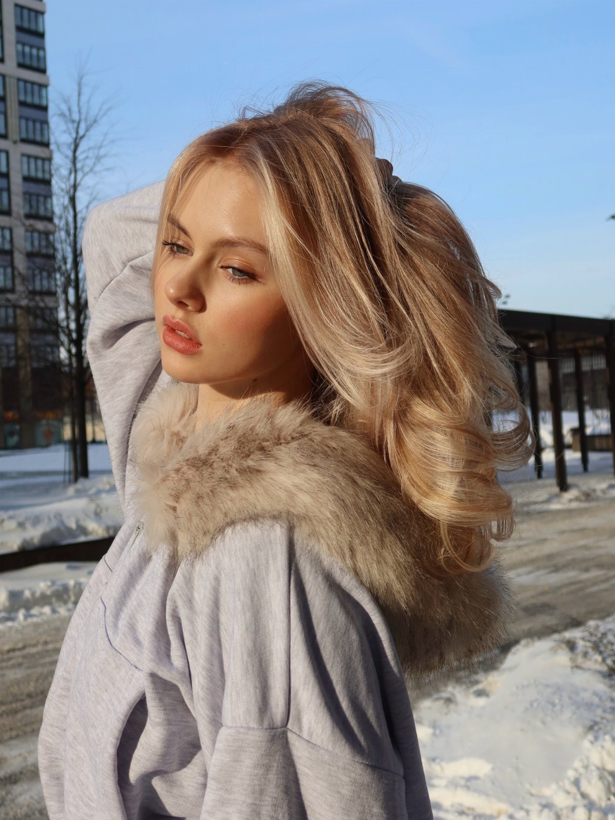 Woman showing glossy sunny honey-blonde waves outdoors in a snowy urban setting