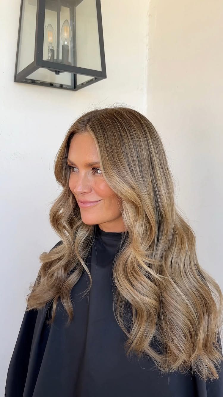 Woman with long light-brown waves and warm blonde face-framing highlights