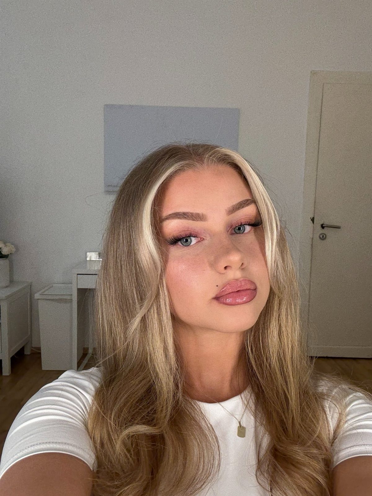 Woman with long warm blonde hair and darker roots wearing a white top
