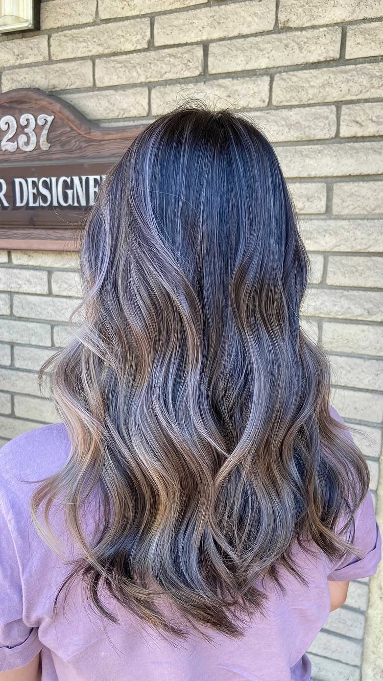 Long wavy dark hair with cool silver highlights against a brick wall