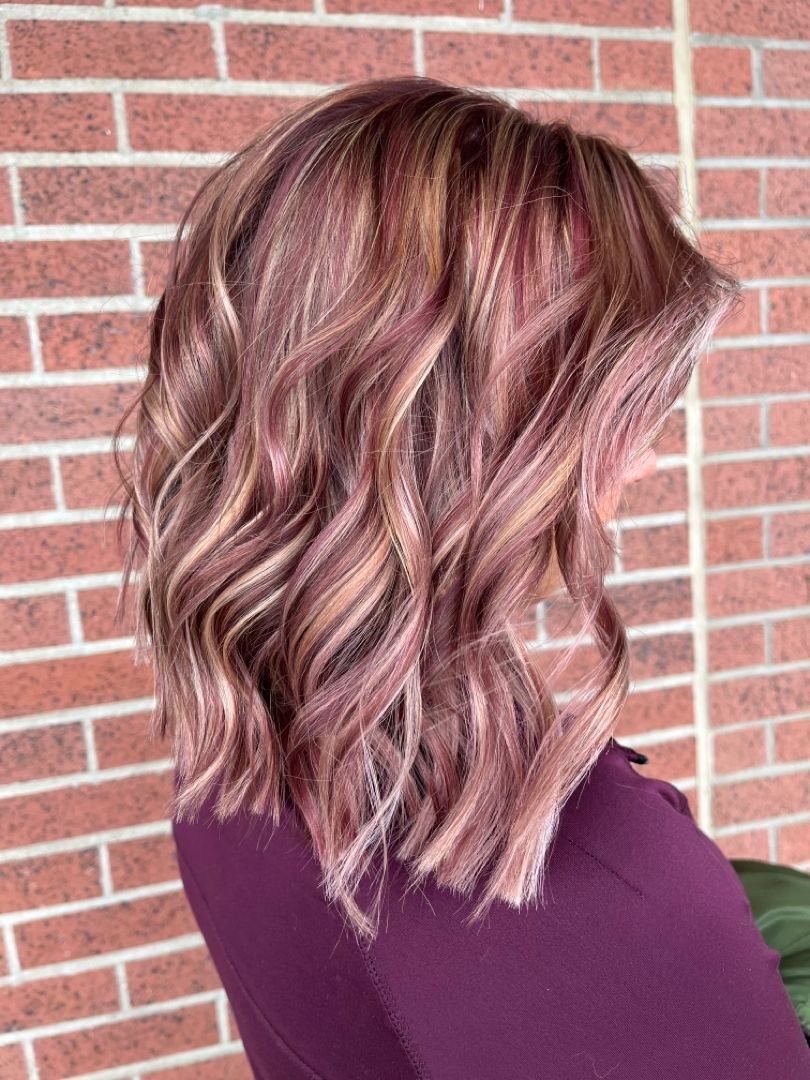 Wavy shoulder-length rose and blonde hair against a red brick wall