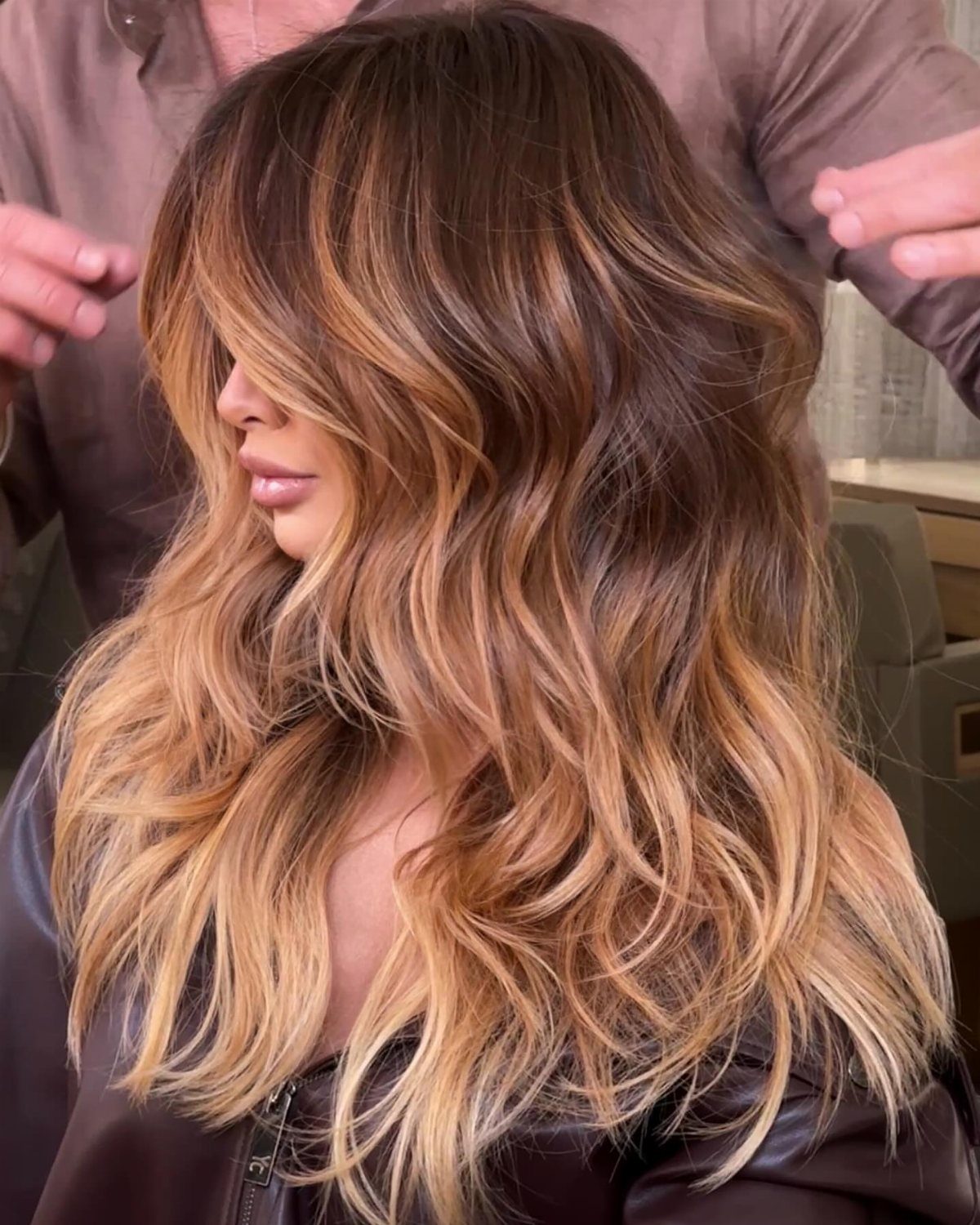 Long wavy dark brown hair blends into caramel and blonde highlighted strands in a salon