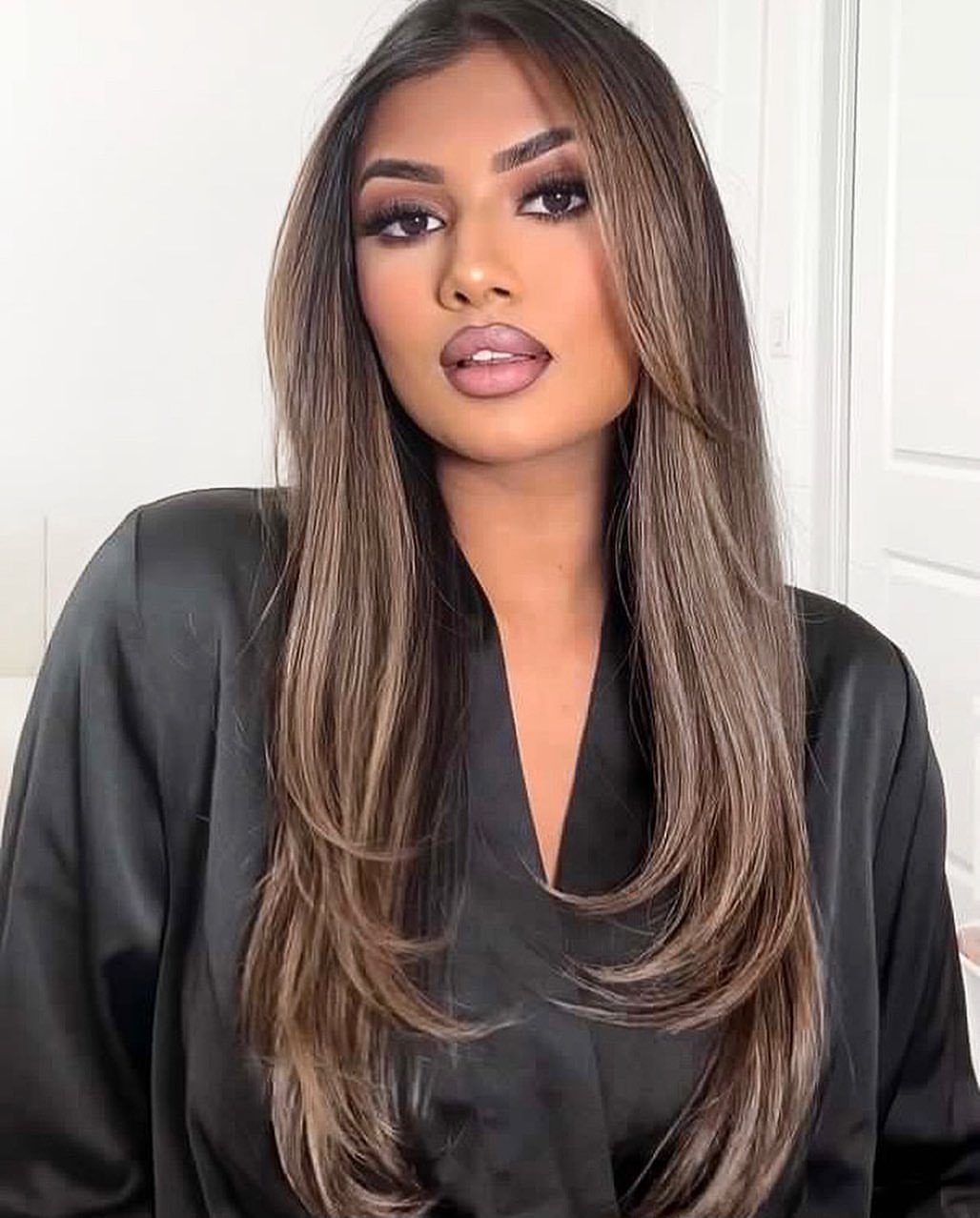 Woman with long dark brown hair and warm highlights, wearing a black blazer