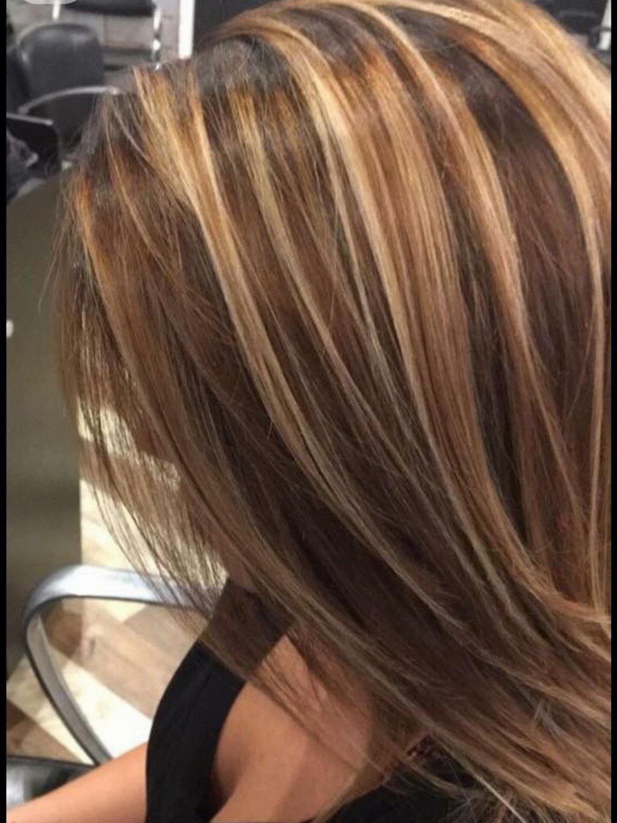 Layered brunette hair with broad honey-blonde ribbons in a salon