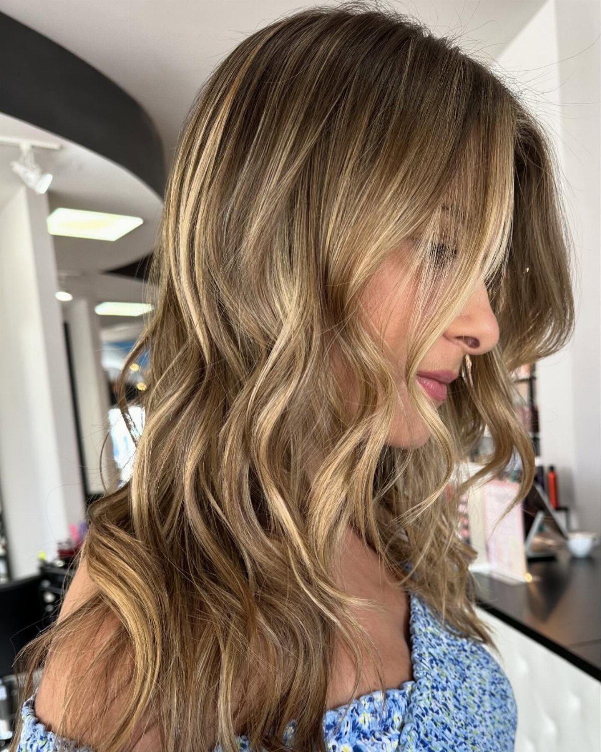 Woman with long dark brown hair and light caramel balayage highlights in a salon