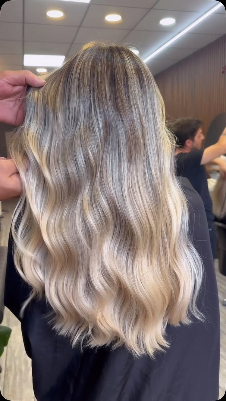 Long wavy hair fades from dark roots to pale blonde ends