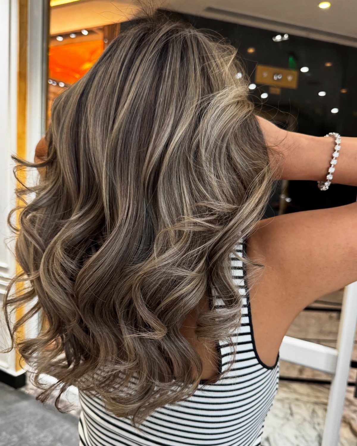 Long dark brown curls with cool ash-blonde highlights shown from behind