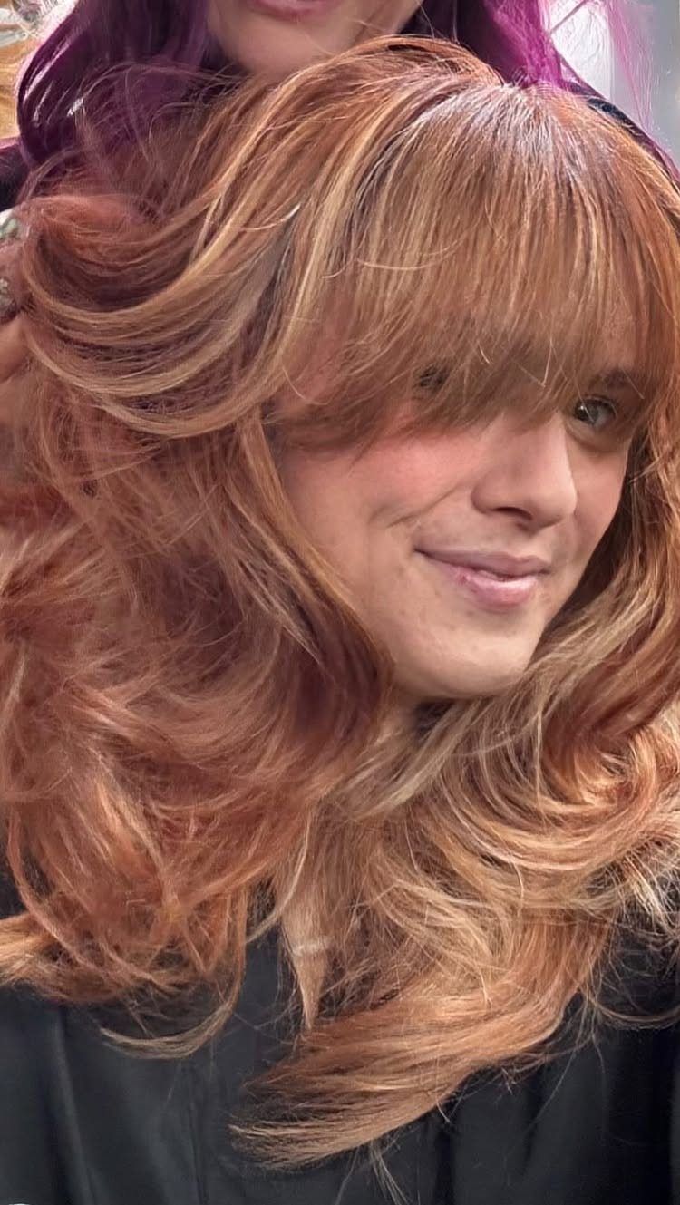 Long copper-red curls show lighter strawberry-blonde highlights and sweeping bangs