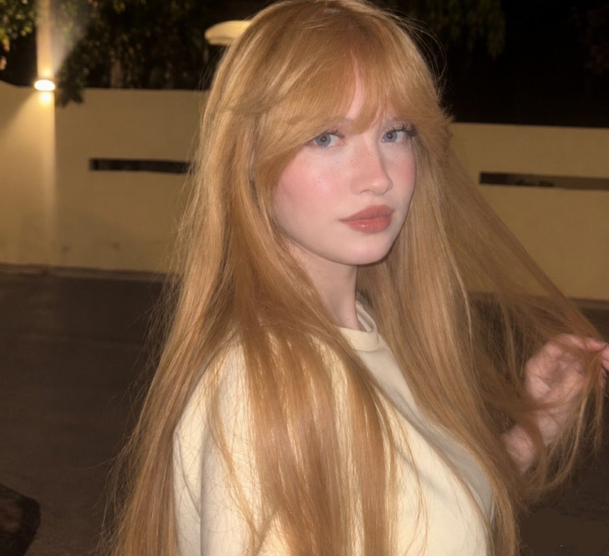 Woman with long, softly blended pastel strawberry-blonde hair and straight bangs