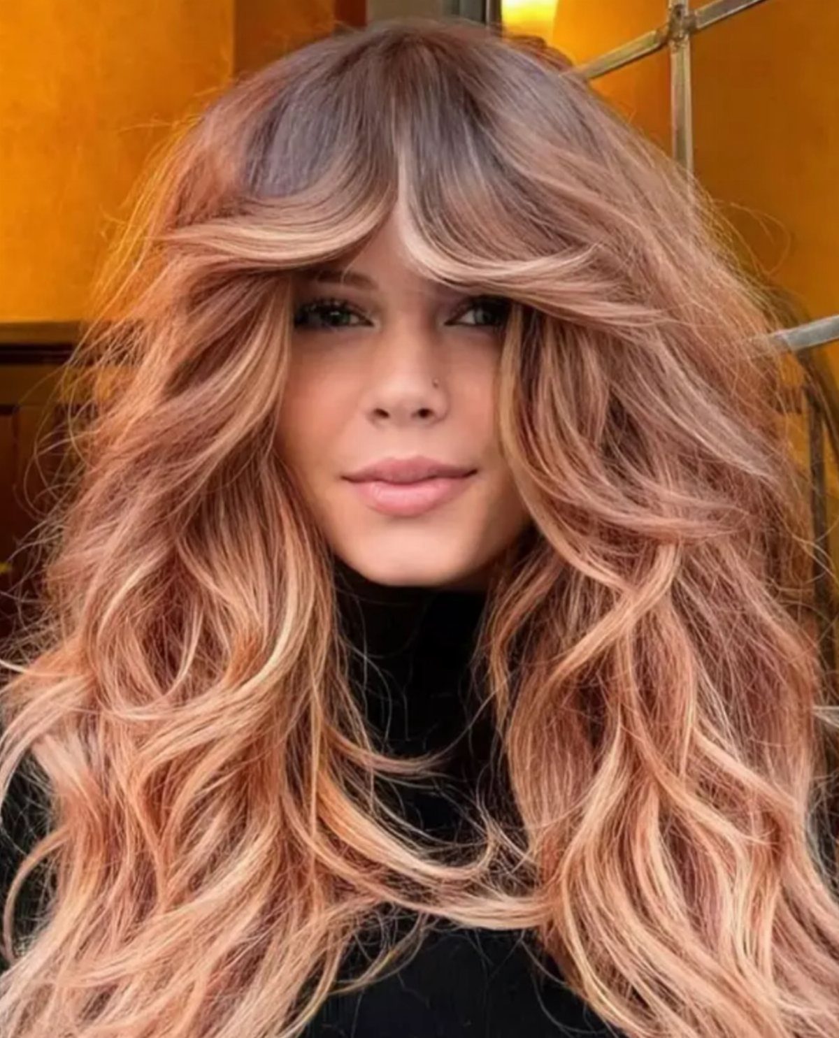 Woman with long wavy strawberry-blonde hair and blonde highlights
