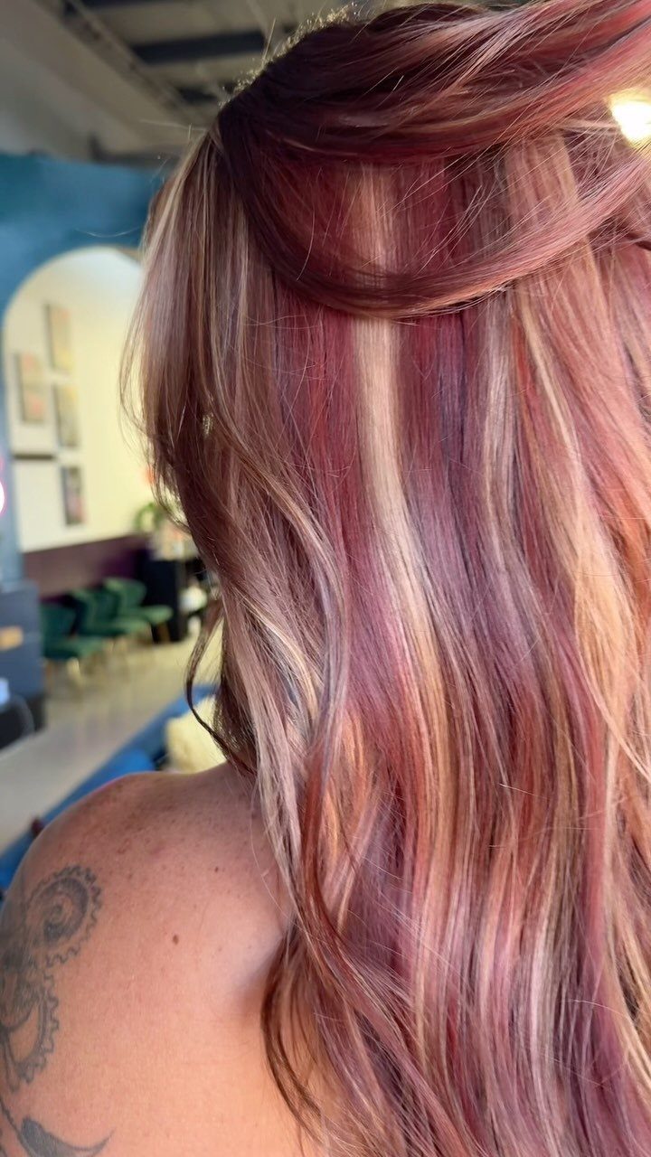 Reddish hair with blonde highlights falls in long waves in a salon