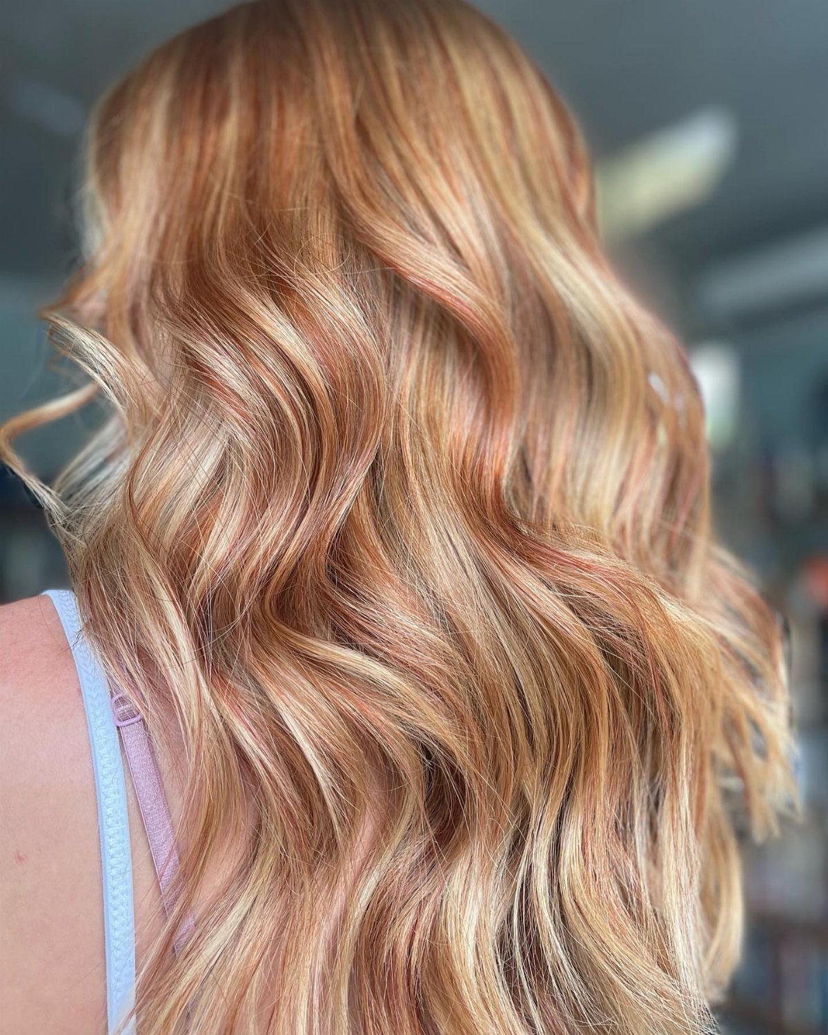 Long copper-red waves with pale blonde highlights against a blurred indoor background