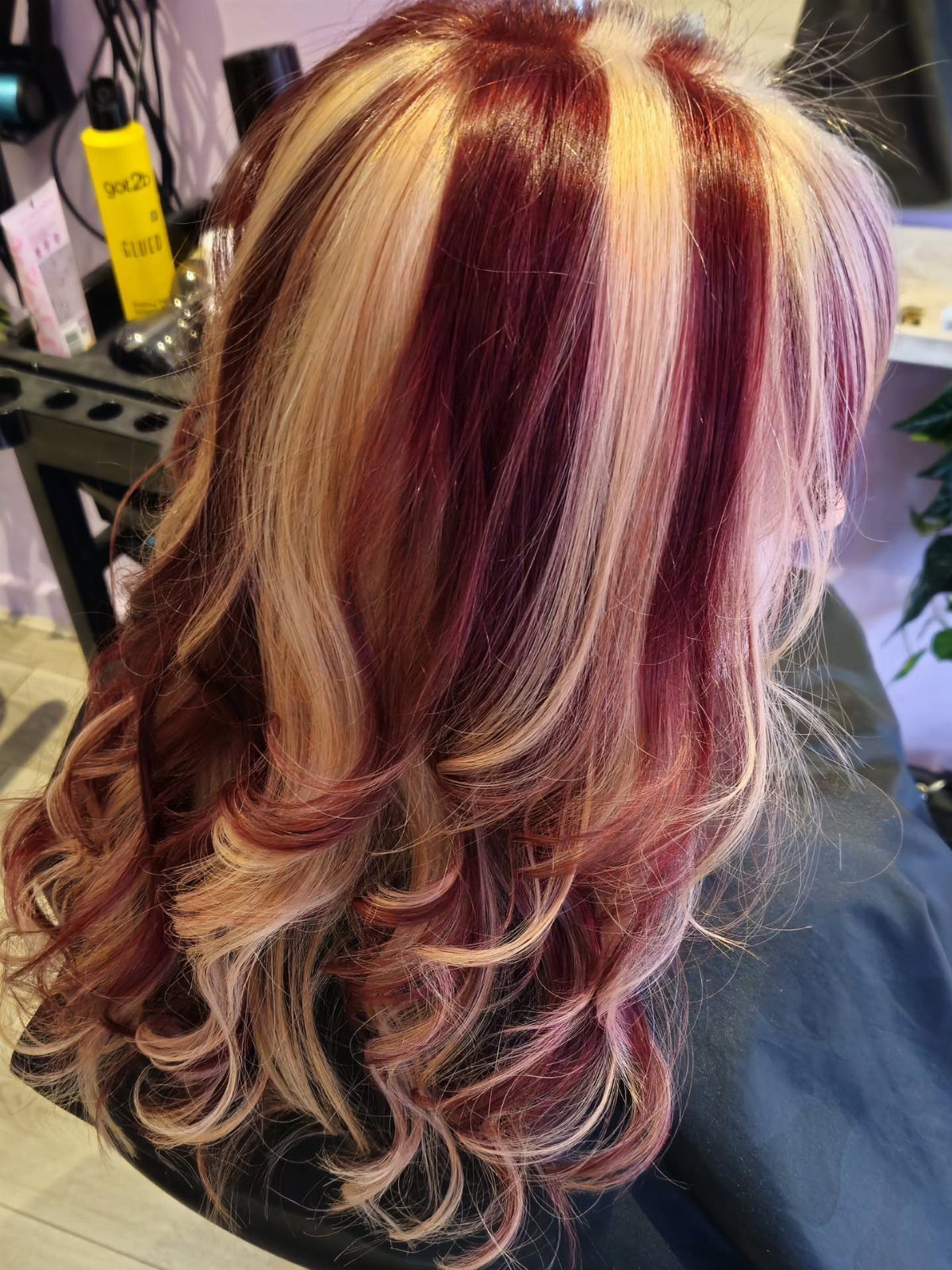 Long curled crimson hair with copper-red and blonde highlights in a salon