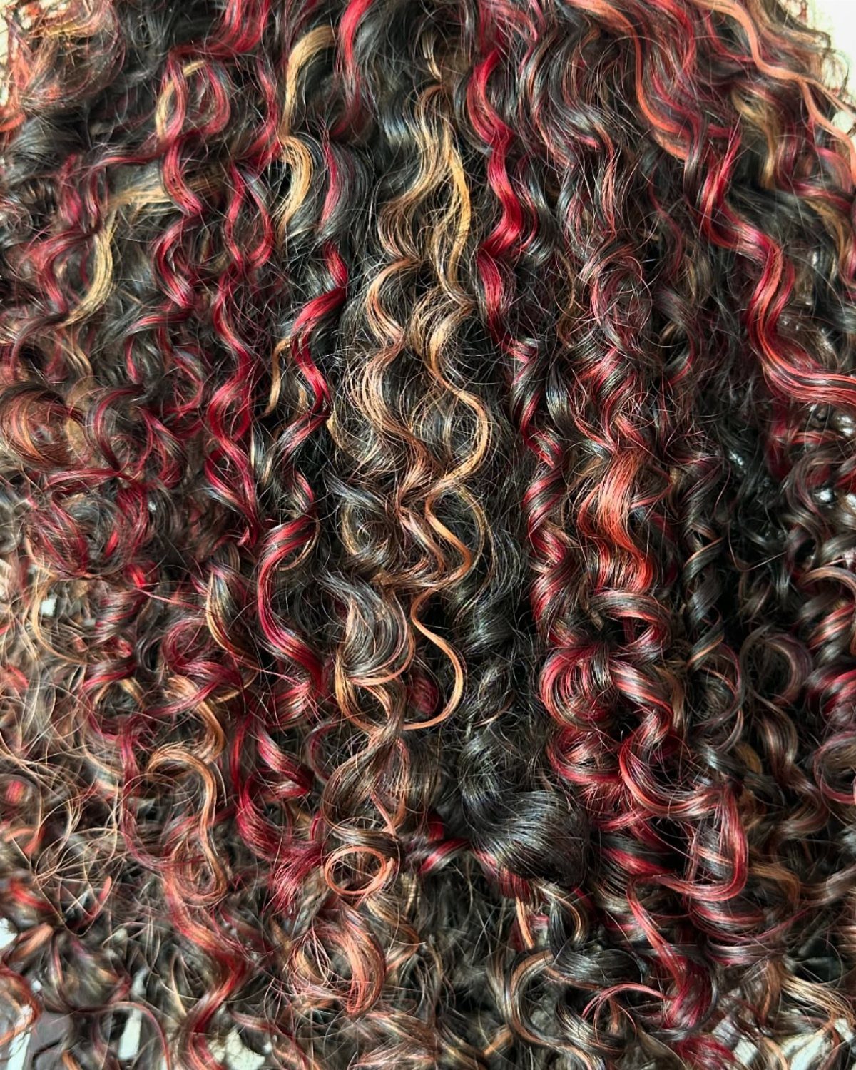 Dark curly hair with vivid red and copper highlights throughout