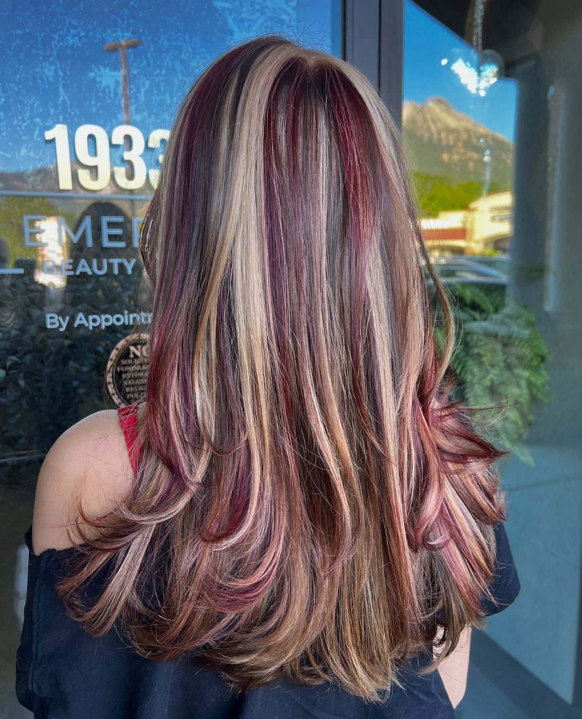 Long layered hair blends burgundy, pink-red, and blonde highlights