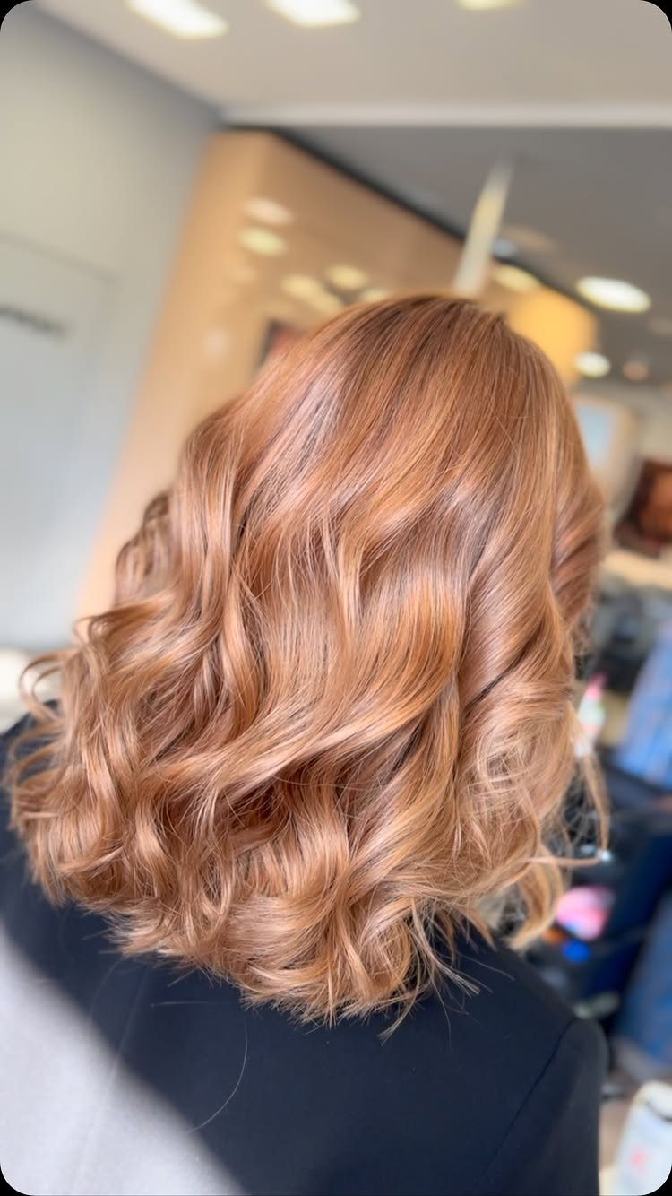 Long curled copper-brown hair with soft blonde highlights styled in salon waves