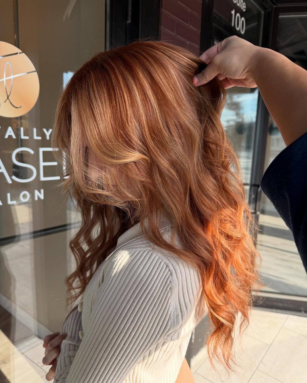 Wavy copper-red hair with blonde highlights being lifted outside a salon