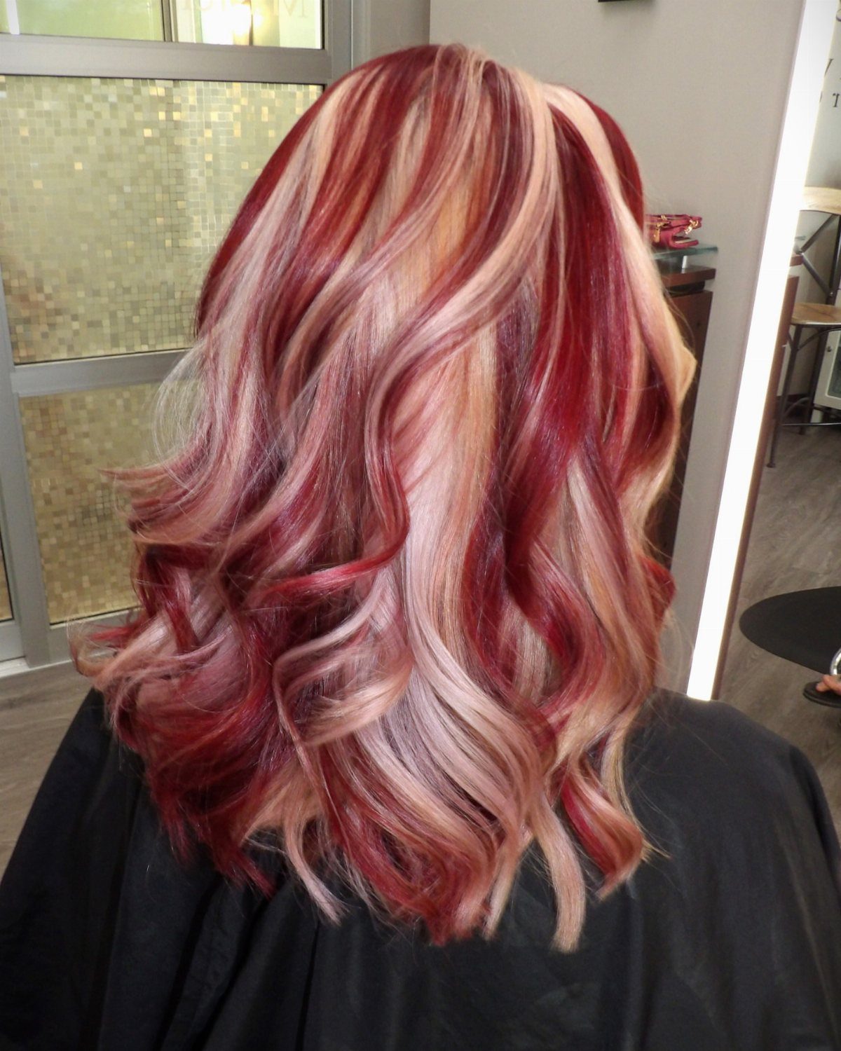 Curled red hair with broad pale blonde highlights in a salon