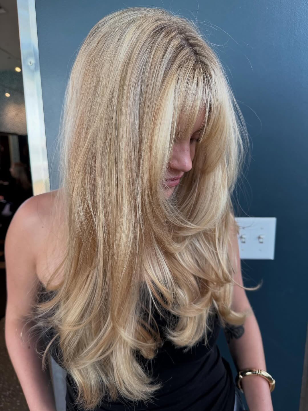 Woman with long blonde layers, bright face-framing highlights, and curtain bangs