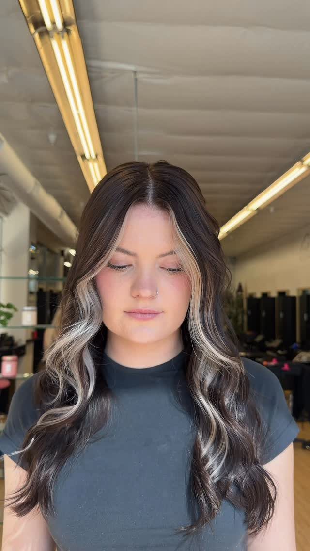 Woman with long dark waves and blonde face-framing sections in a salon
