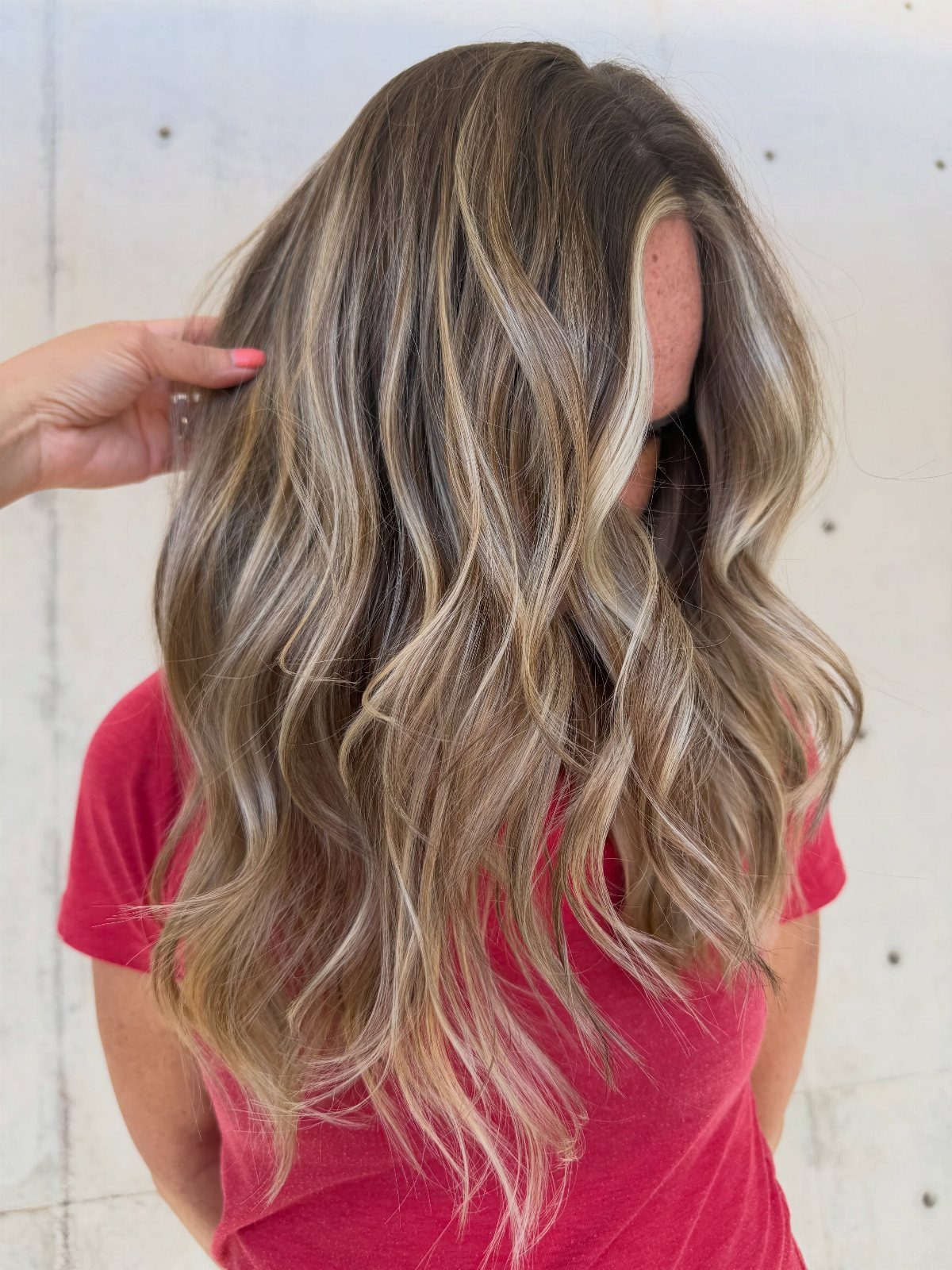 Brunette waves with bright blonde face-framing highlights against a pale wall