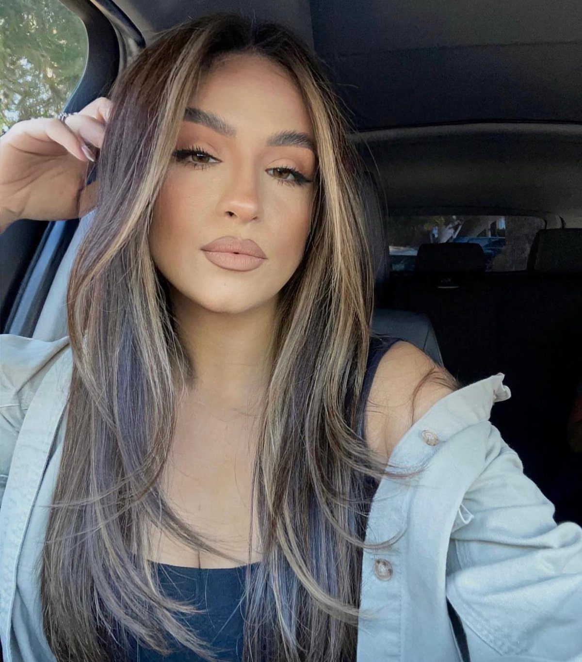 Woman with long chestnut hair and blonde face-framing highlights posing in a car