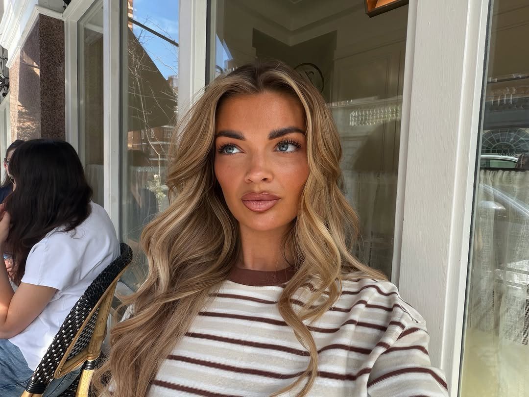 Woman with wavy brunette hair and thick cream-blonde highlights framing her face