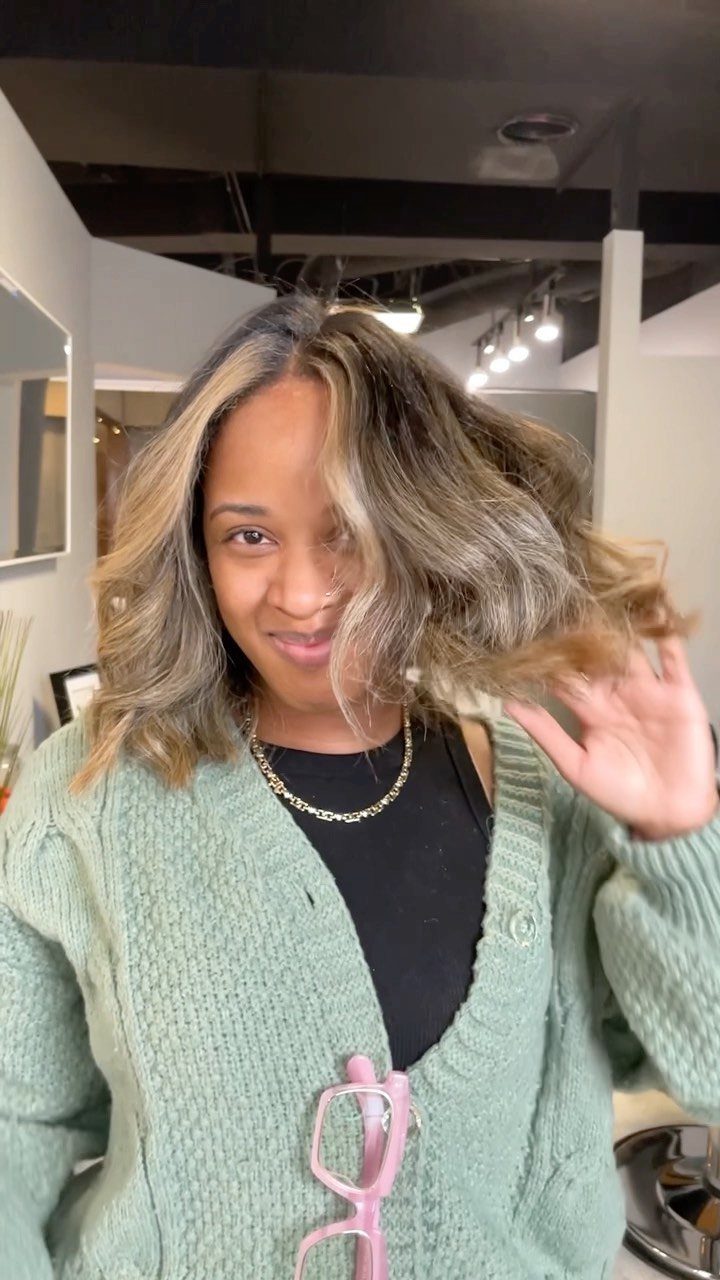 Woman showing wavy brunette hair with subtle blonde face-framing highlights in a salon