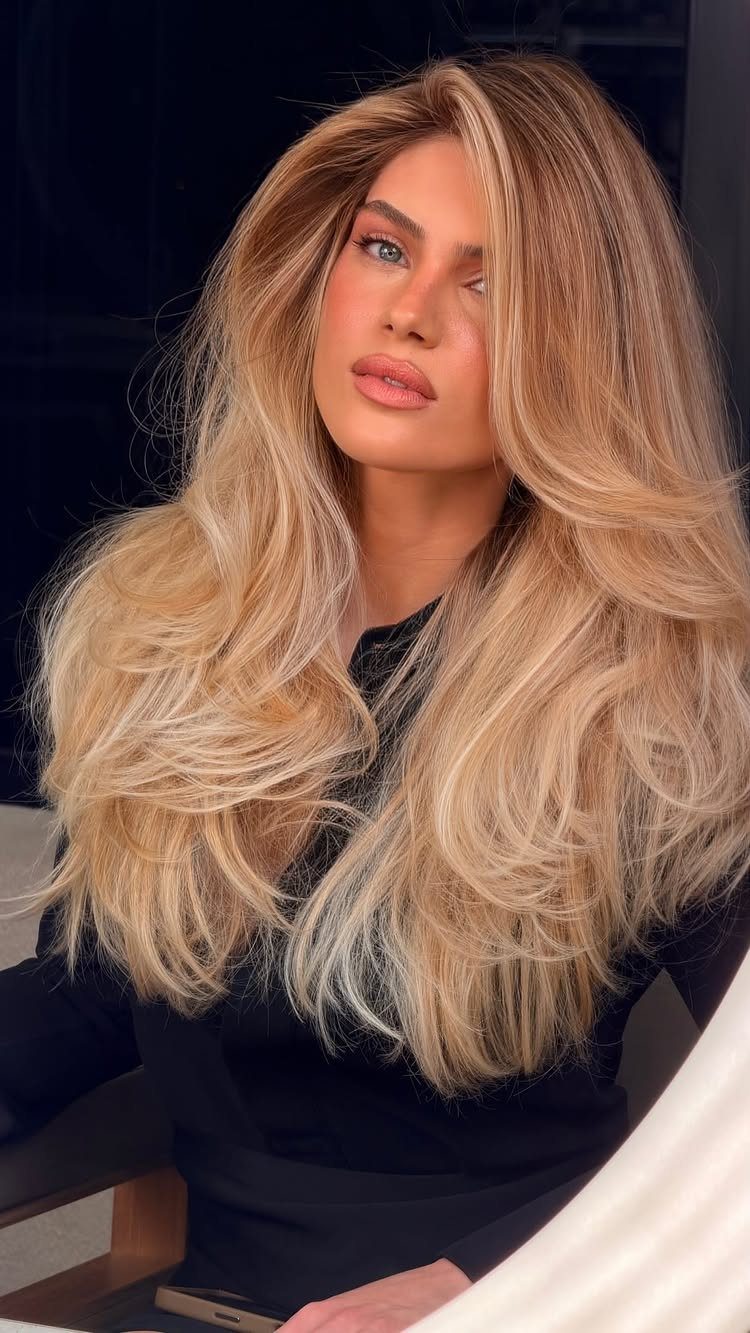 Woman with long blonde hair, caramel-toned roots, and voluminous soft waves
