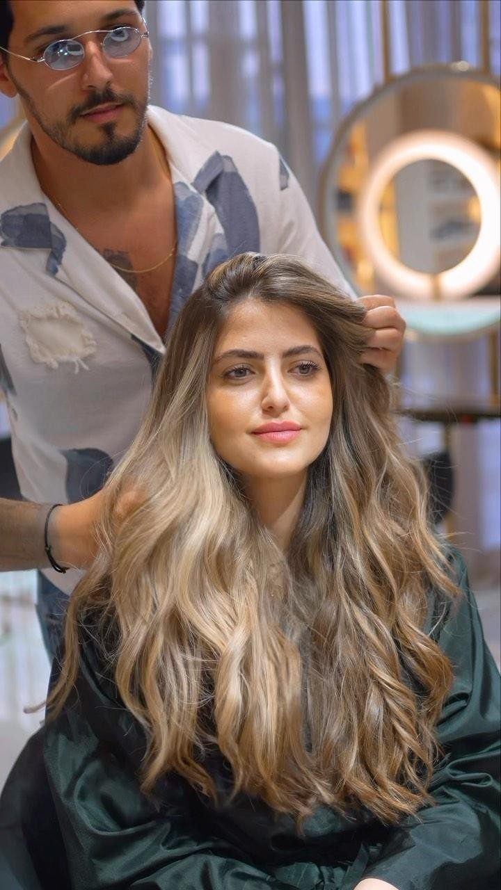 Long wavy blonde hair with caramel tones styled in a salon chair