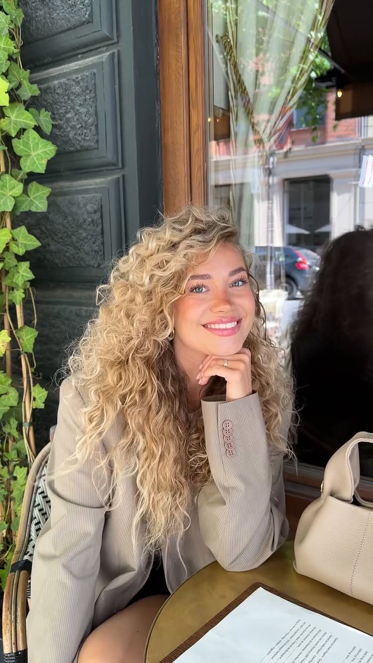 Woman with long blonde curls smiling at a café table